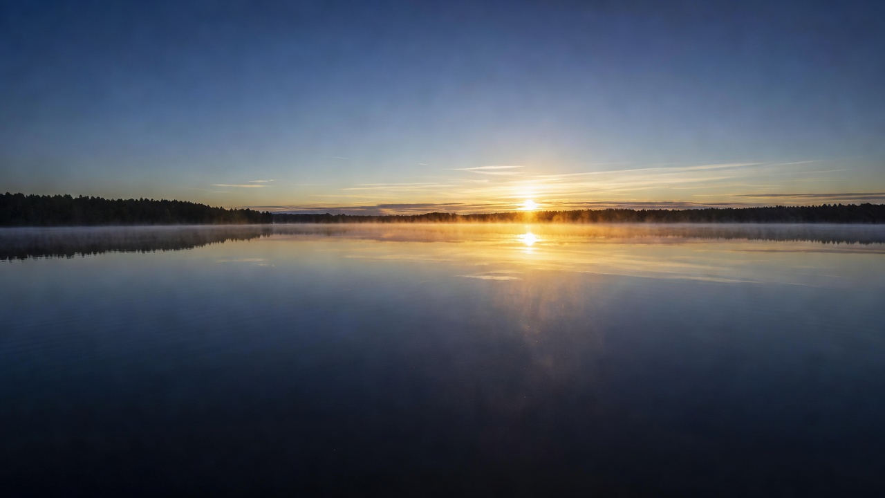First light breaking over a still lake with mist rising, deep navy water reflecting golden dawn light, serene, vast, contemplative, editorial quality, no people